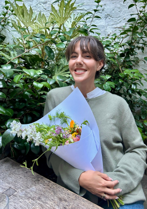 A women with brown hair holds a bunch of flowers smiling